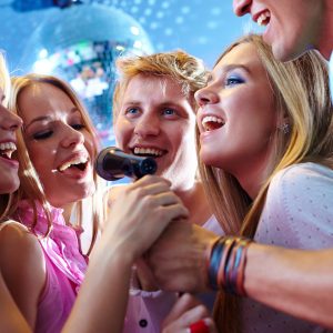 Young men and women holding onto a microphone and happily singing. Goodfella's hosts a weekly karaoke event.